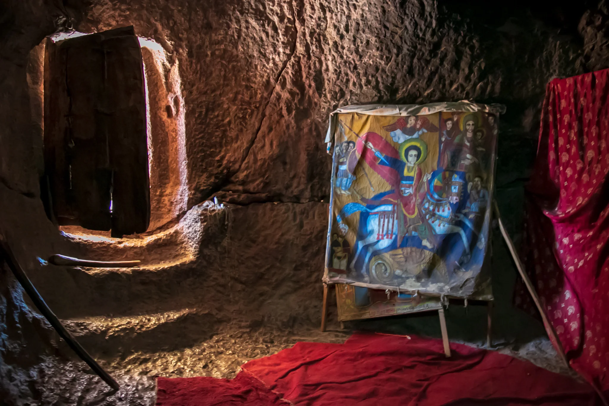 A canvas painting of dragon-slaying St. George near the stone-carved entrance of a cave-like Lalibela church. // photo © Kim I. Mott