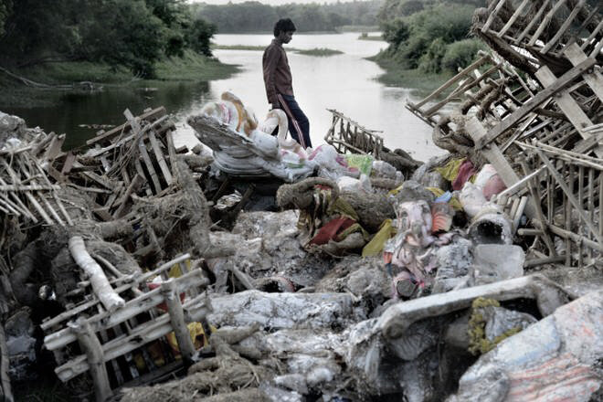  Person crossing a water body with post immersion waste piled up next to the bridge 