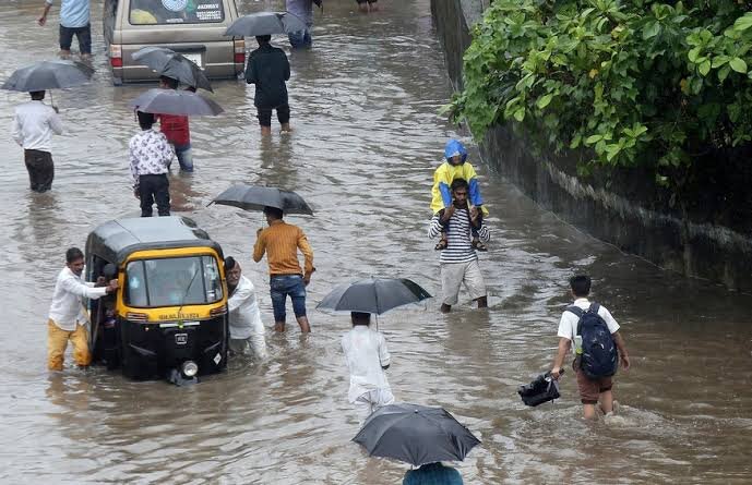  People wading through a flooded street with some dragging an auto along and a man carrying his child on his shoulders to keep him away from the floods 