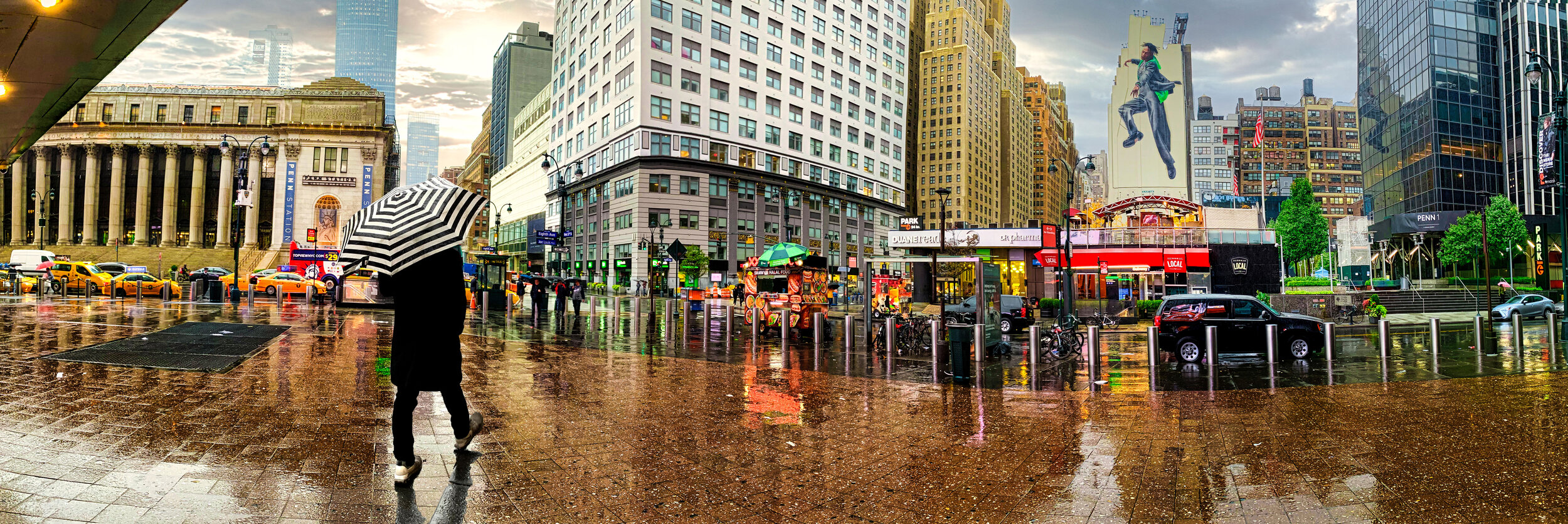 City street scene on a rainy day with people holding umbrellas, reflecting wet pavement, tall buildings, billboards, and yellow taxis.