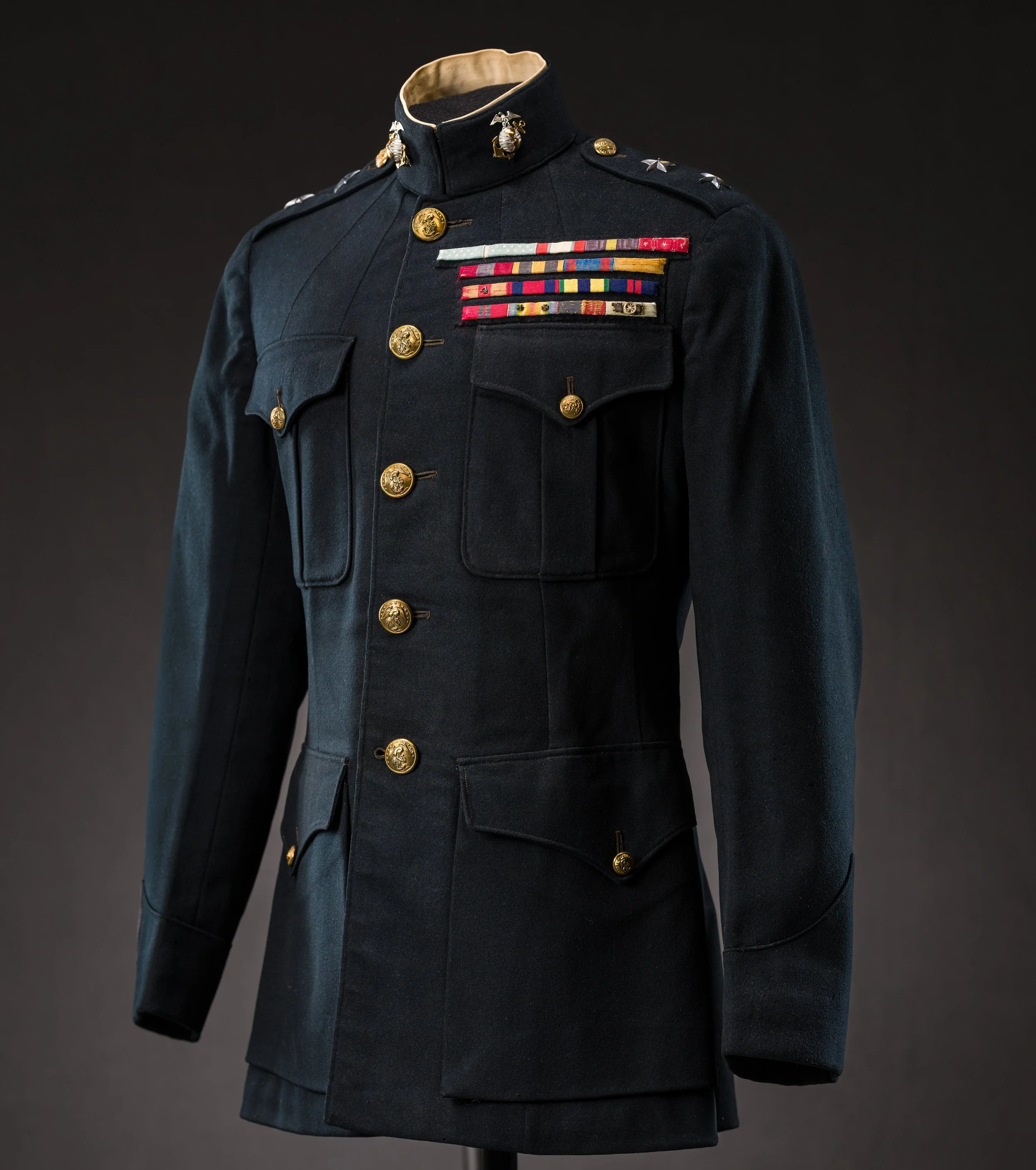 A vintage military dress uniform with gold buttons, shoulder insignia, and various colorful ribbons on the chest, displayed against a dark background.