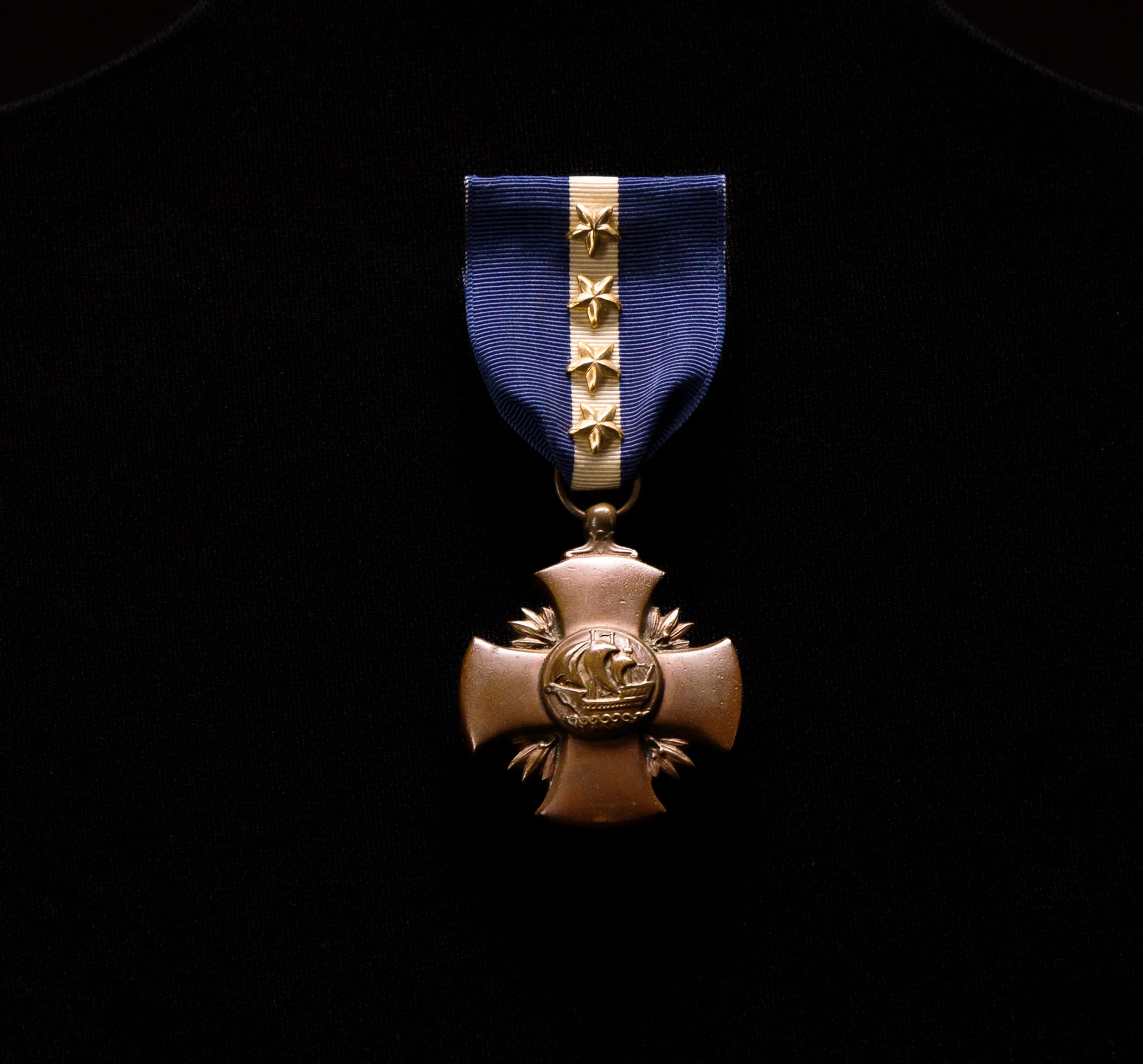 Medal with a blue and white ribbon and three gold stars, bearing a emblem of a ship inside a wreath.