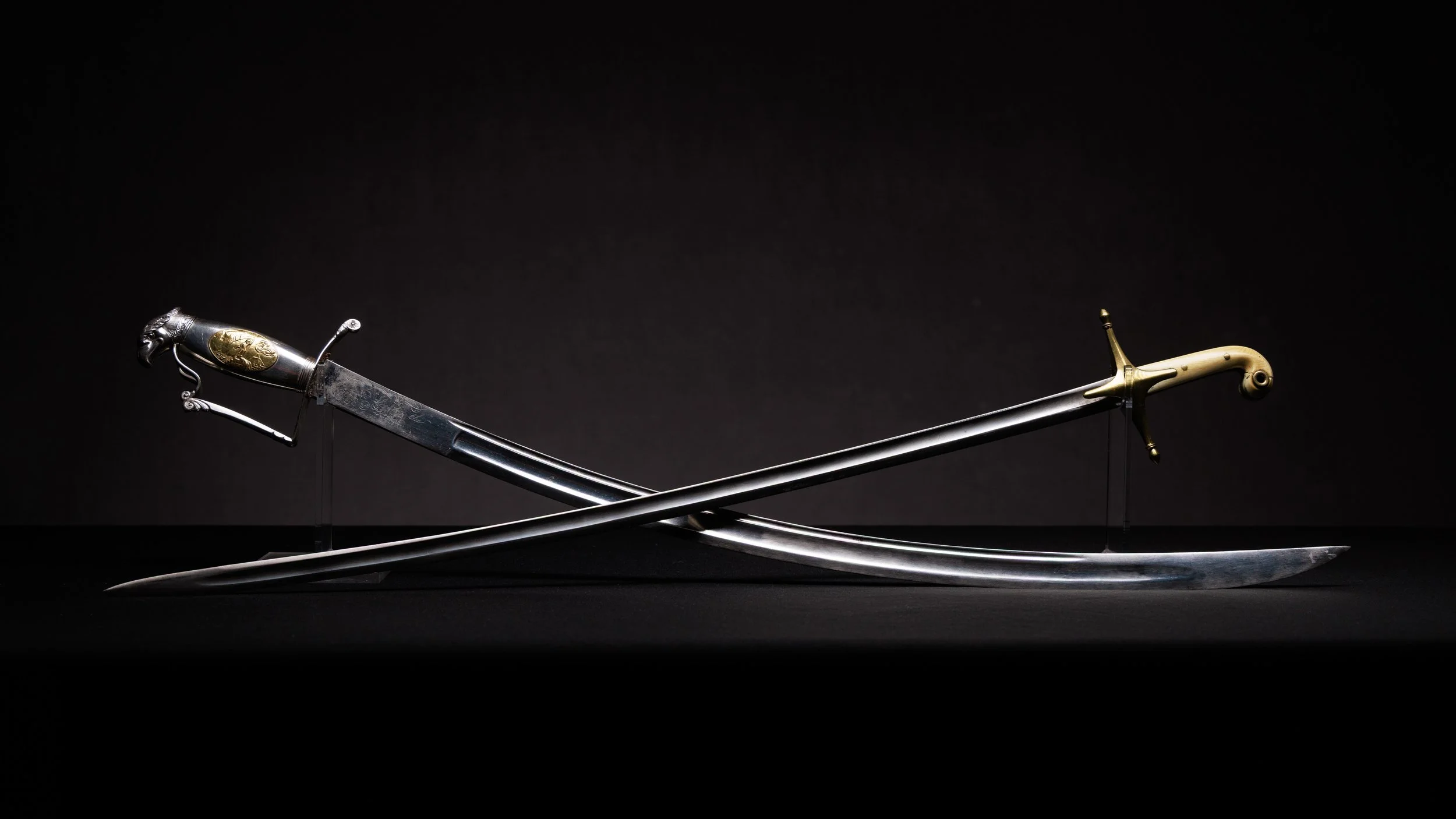 Two ornate swords with animal-shaped hilts, crossed and displayed on a black background.