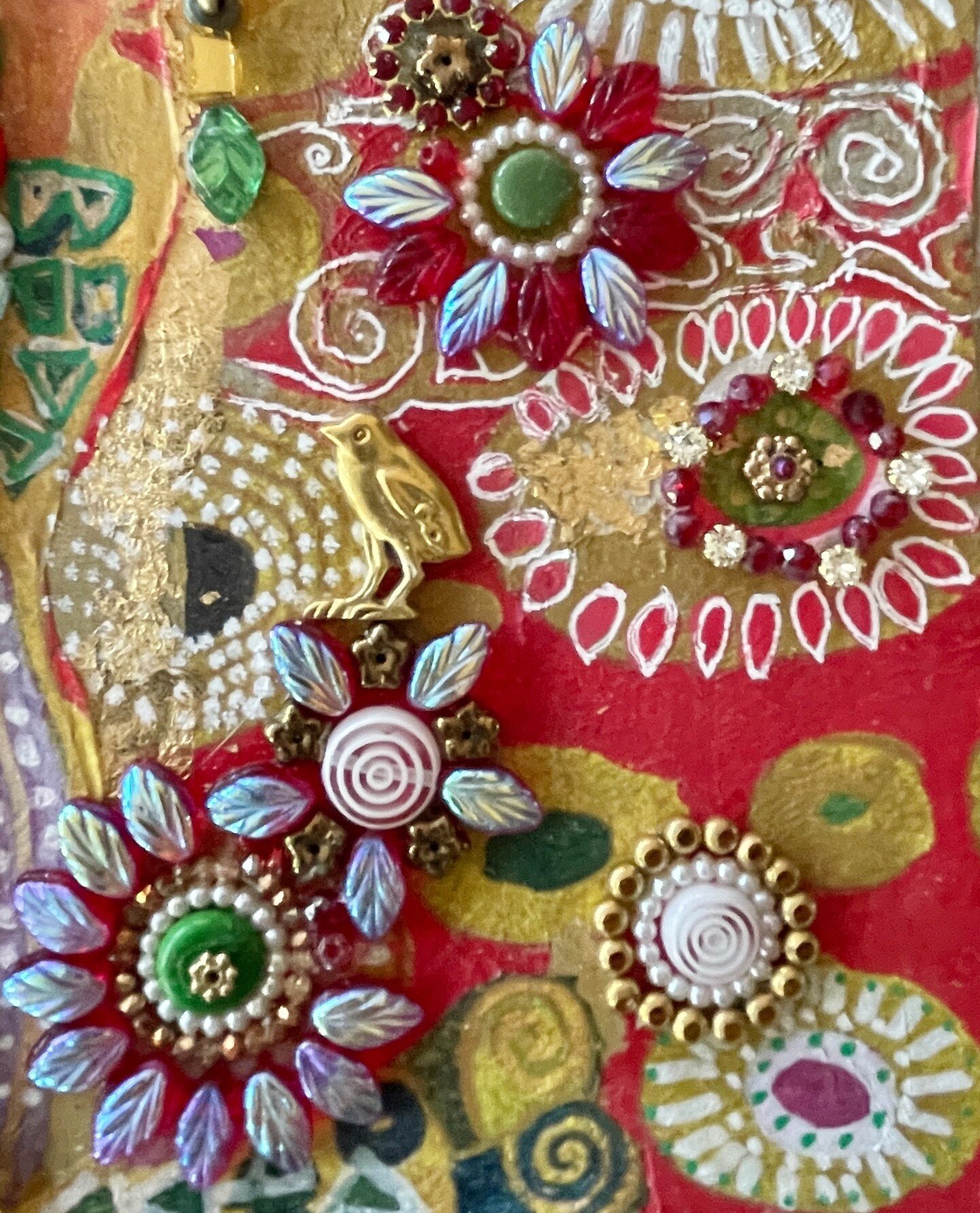 A closeup of a mixed media mosaic. The base is covered with a paper napkin with a Klimt design that I purchased at the MFA in Boston. I painted over portions of the design and then mosaicked over the piece with glass, beads and recycled jewelry. What