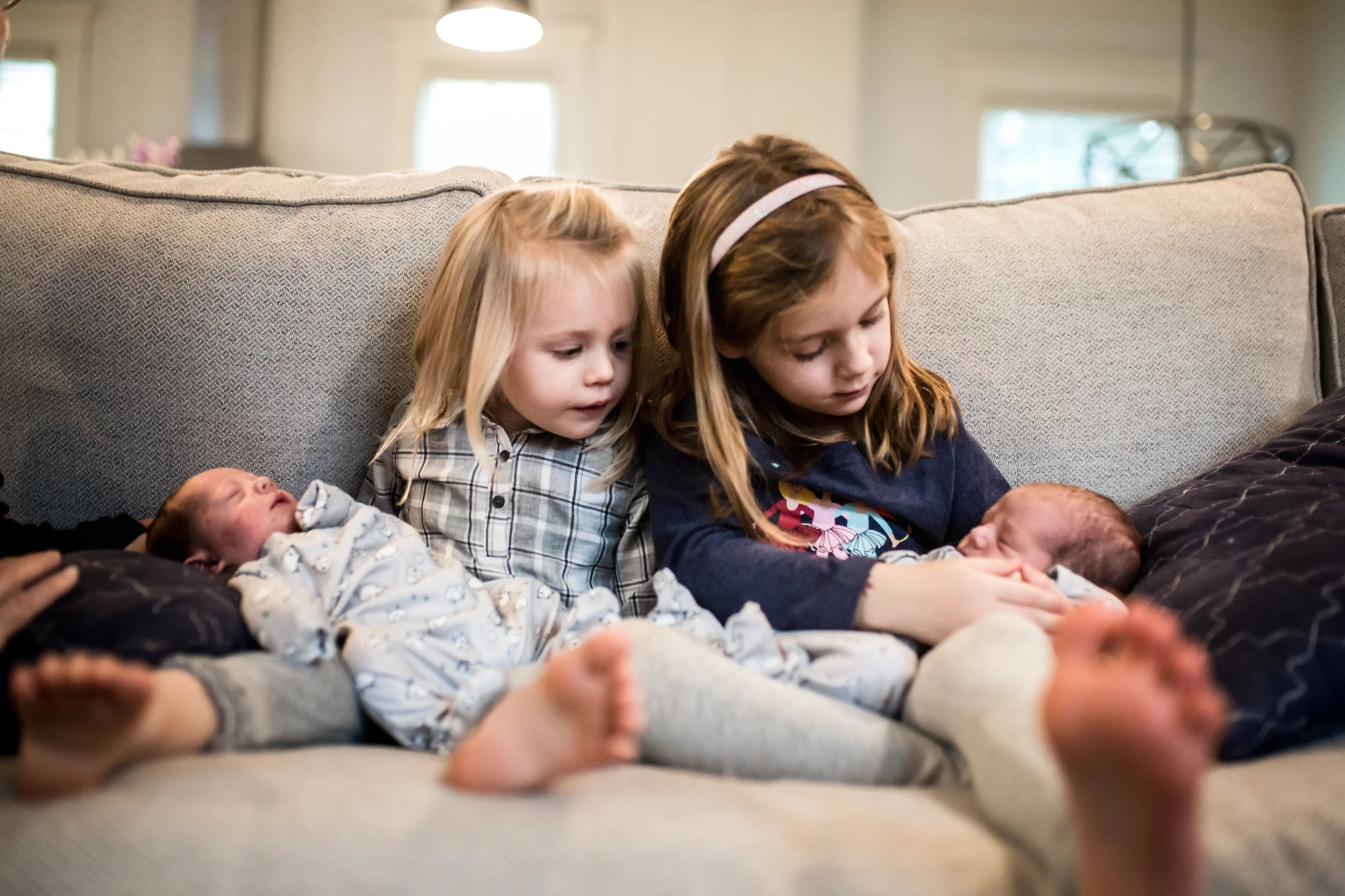 Sisters sitting on the couch at home with their newborn twin sisters sitting in their laps