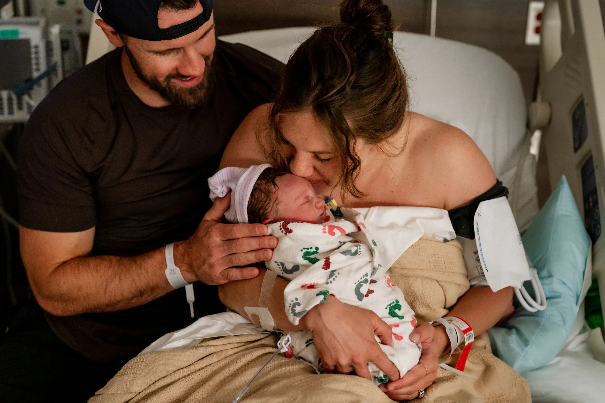 Parents snuggling their newborn baby in bed, as mom kisses the baby, at Piedmont Hospital in Atlanta