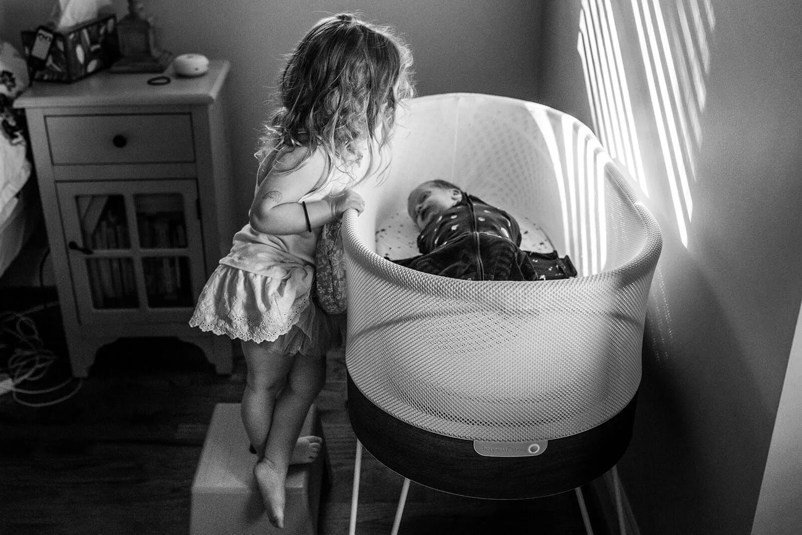 LIttle girl looking into the bassinet of her newborn baby brother at home