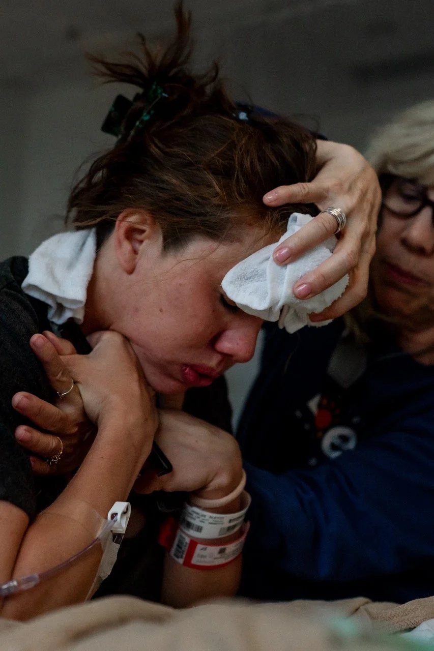 Mother in labor at the Piedmont Hospital, leaning on the bed while her mom holds a washcloth on her forehead