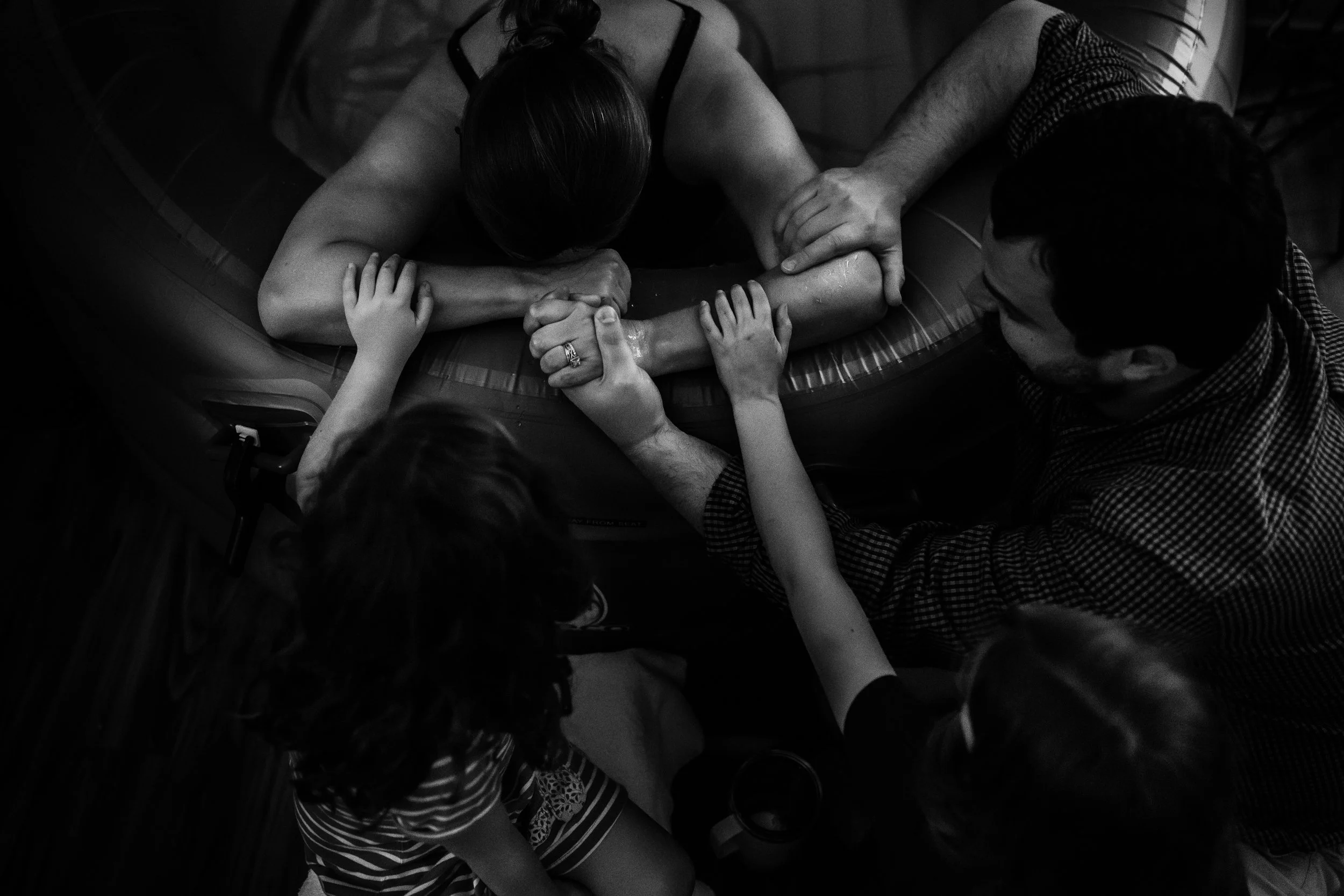 Mother birthing in a birth pool with the support of her husband and kids next to her at Atlanta Birth Center