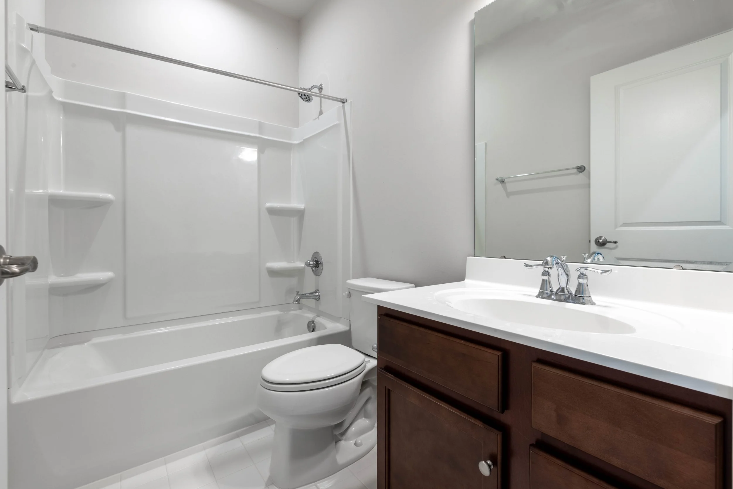 Modern white bathroom with a bathtub and shower, toilet, vanity with sink and faucet, large mirror, and towel rail.