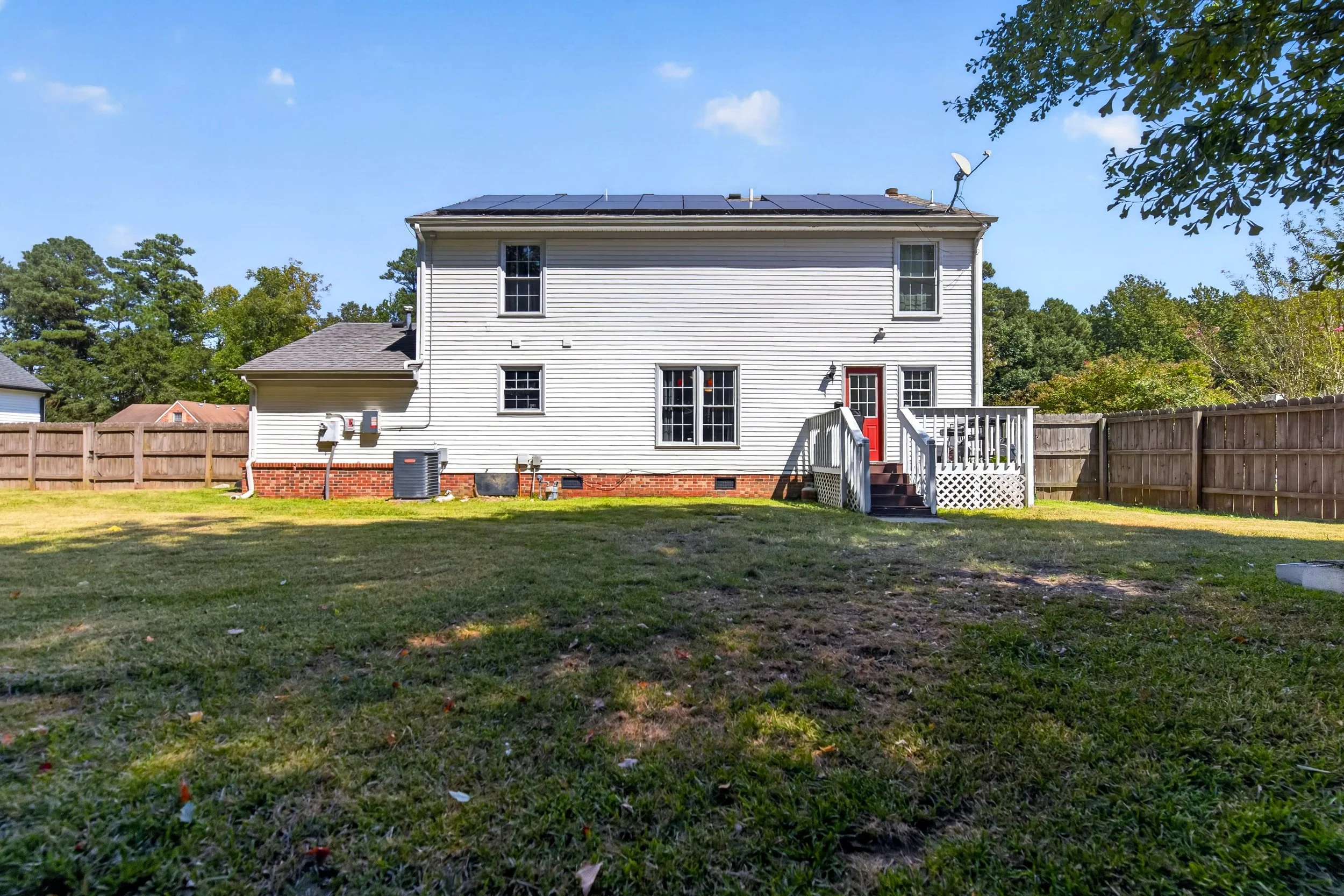 A wide backyard view shows the open lawn, mature trees and rear exterior of 811 Haskins Drive.