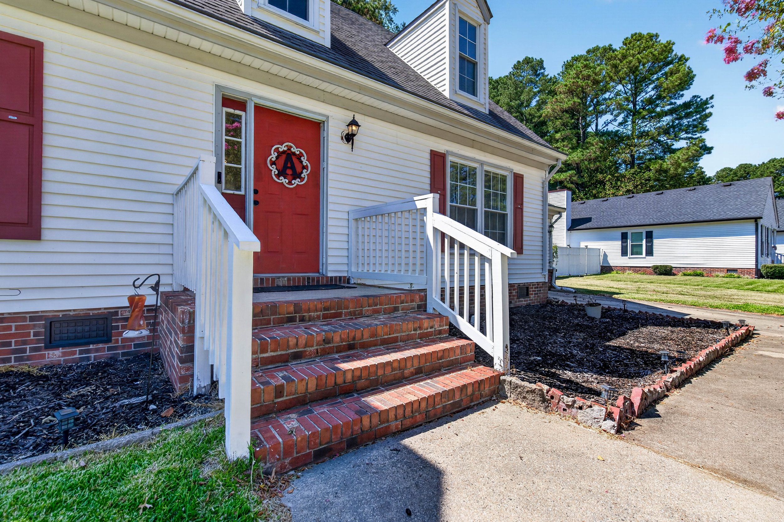 Brick steps lead to the red front door, with red shutters and landscaped beds along the exterior.