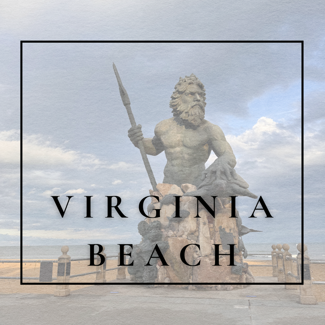 Statue of a muscular bearded man holding a spear, sitting on a rock, located at Virginia Beach with the ocean and cloudy sky in the background.