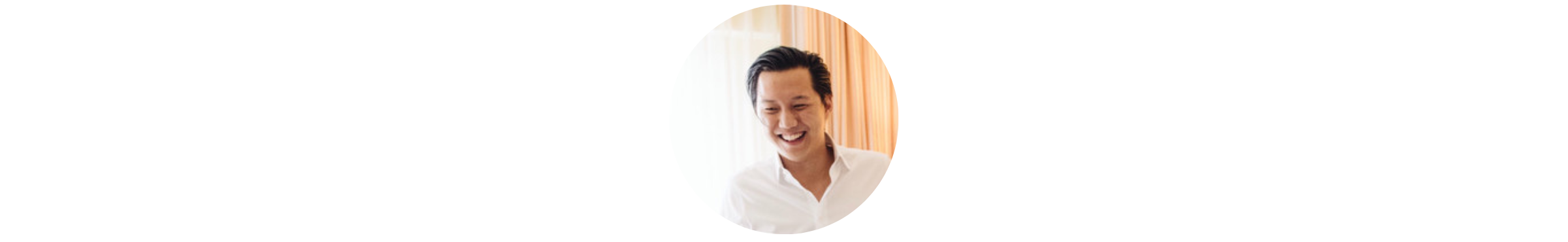 A smiling man with dark hair in a white shirt looking down.