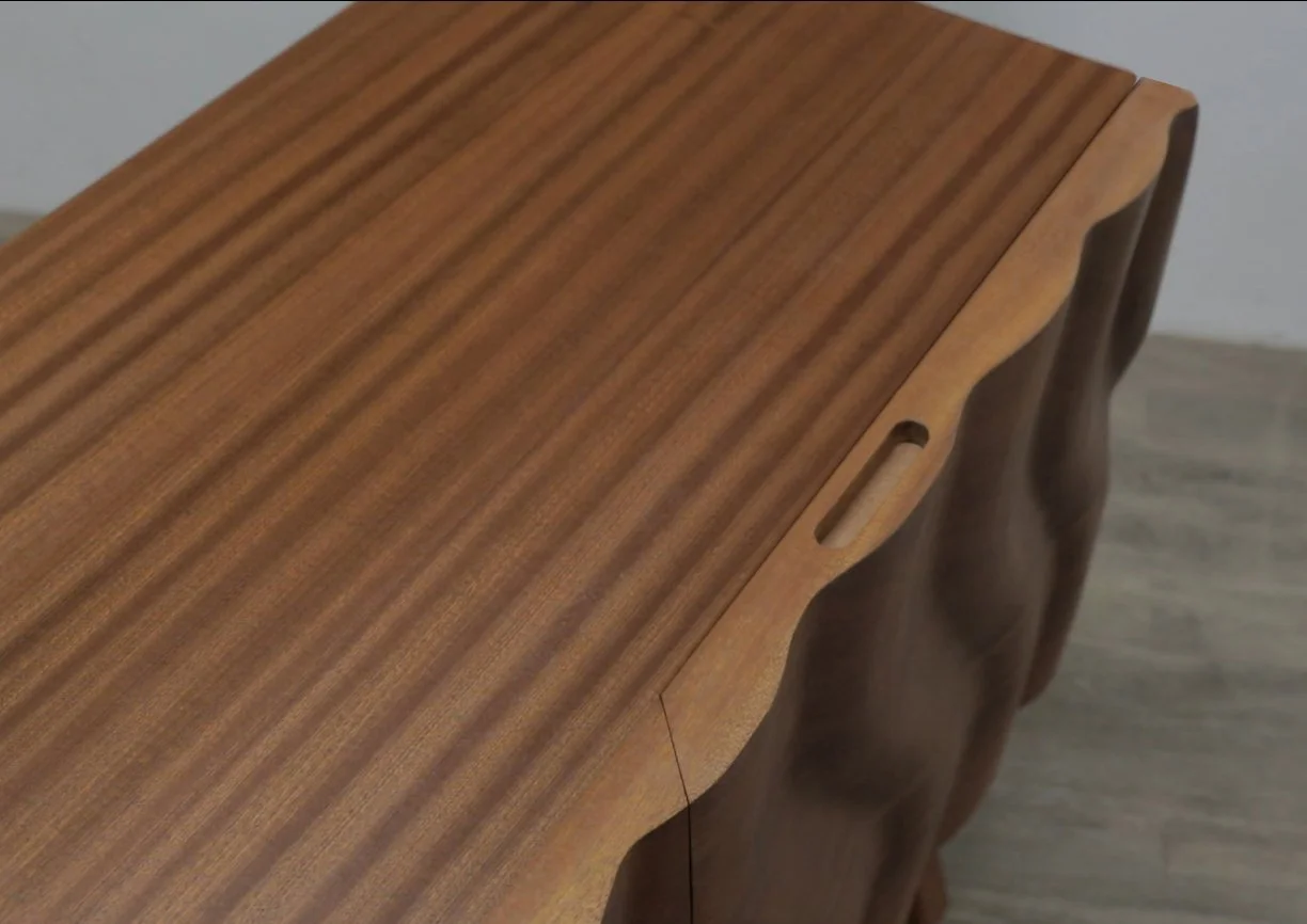Close-up of a wooden furniture piece with a smooth, polished surface and carved handle opening
