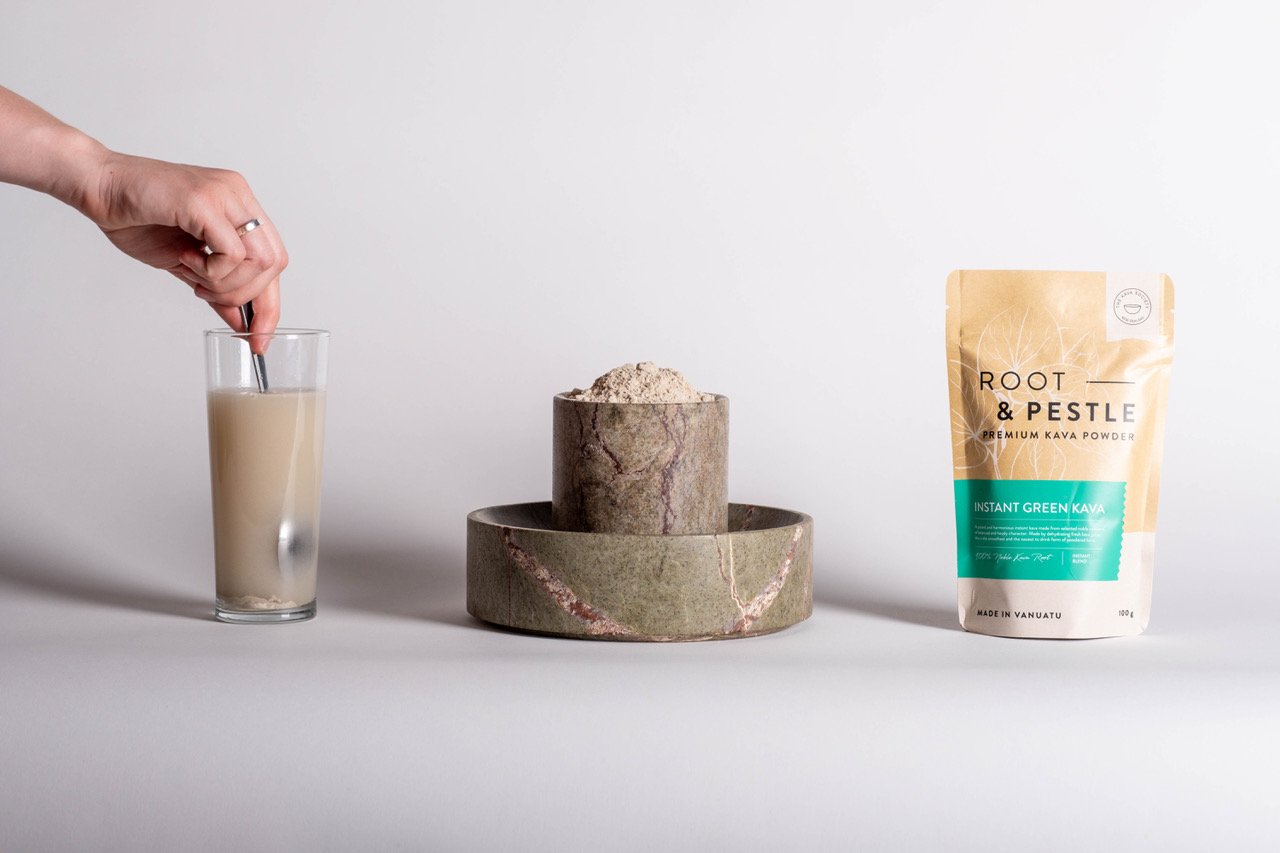 A hand stirring a glass of liquid, a bowl filled with kava powder, and a bag labeled "Root & Pestle Premium Kava Powder" on a light background.