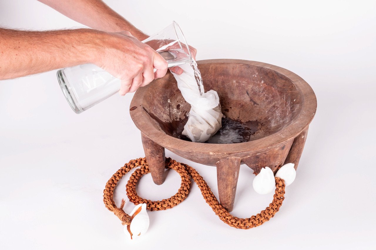 Pouring water into a wooden kava bowl with a strainer and a decorative rope with shells on it.