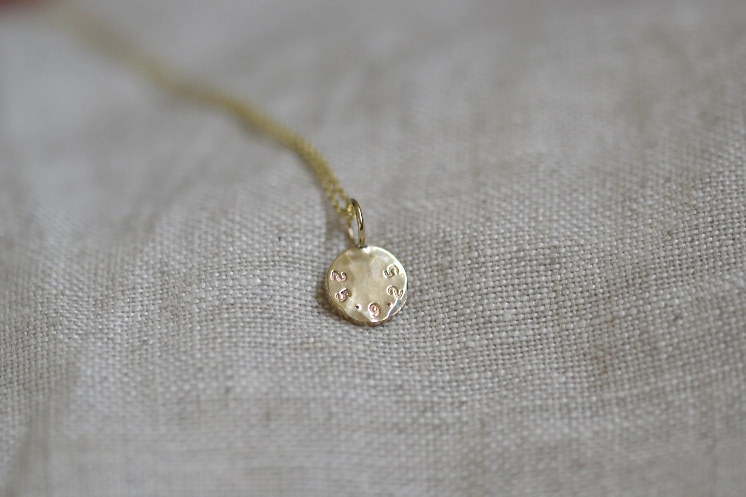 A lightly hammered gold disc necklace with stamped  numbers