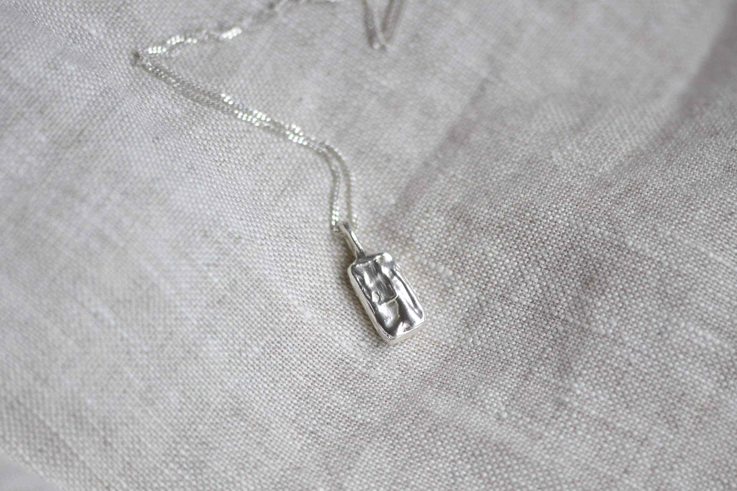 Boxy shaped organic silver necklace on a linen background