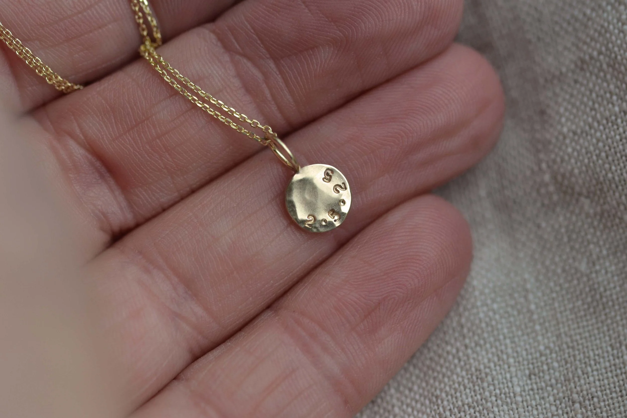 A hand holding a small hammered 9ct gold disc necklace with engraving