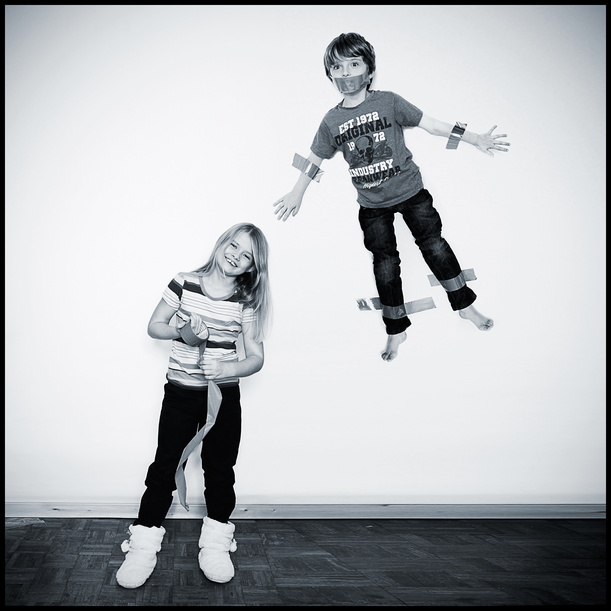 funny portrait of sister taping brother to the wall