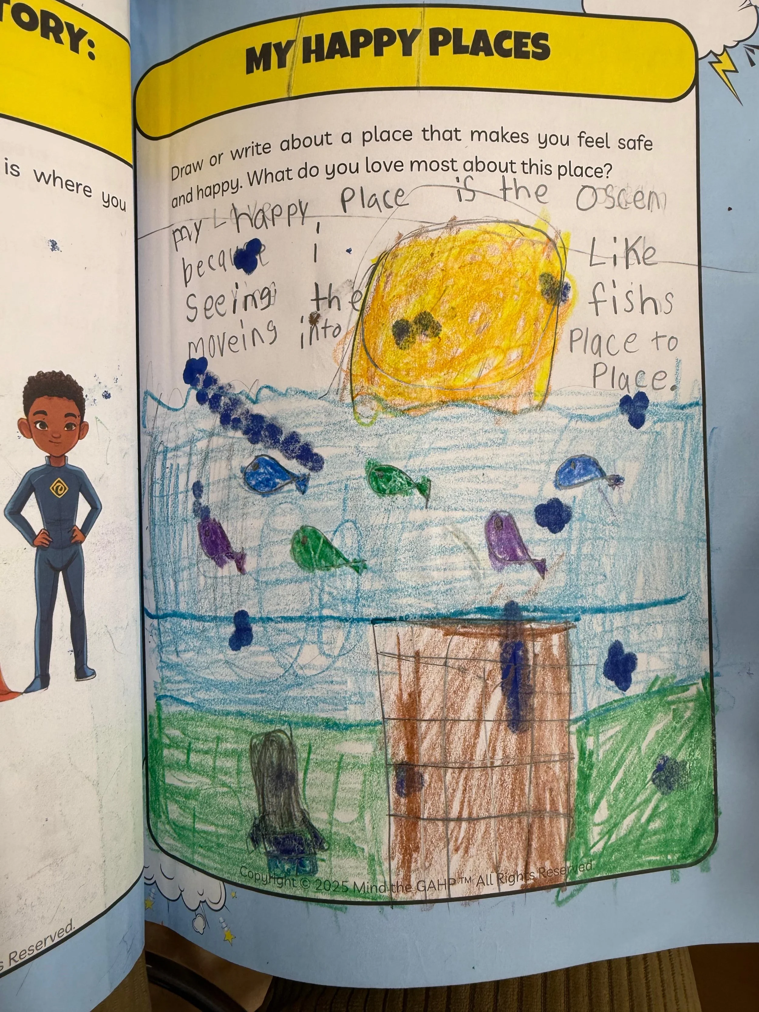 A child's drawing of an ocean scene with a large yellow and orange fish, colorful small fish, and a coral-colored sea floor. There is a handwritten description about a place that makes the child feel safe and happy, indicating it is an ocean where th