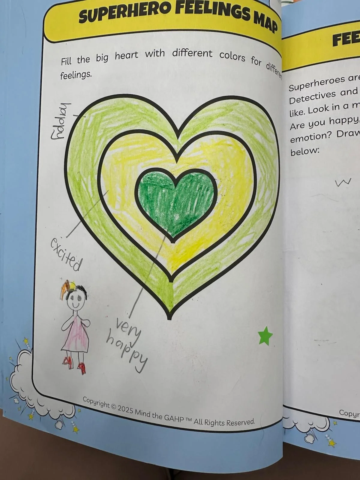 A drawing of a large colorful heart with concentric layers of green and yellow, designed as a 'Superhero Feelings Map,' with handwritten notes and a small doodle of a happy girl outside the heart.