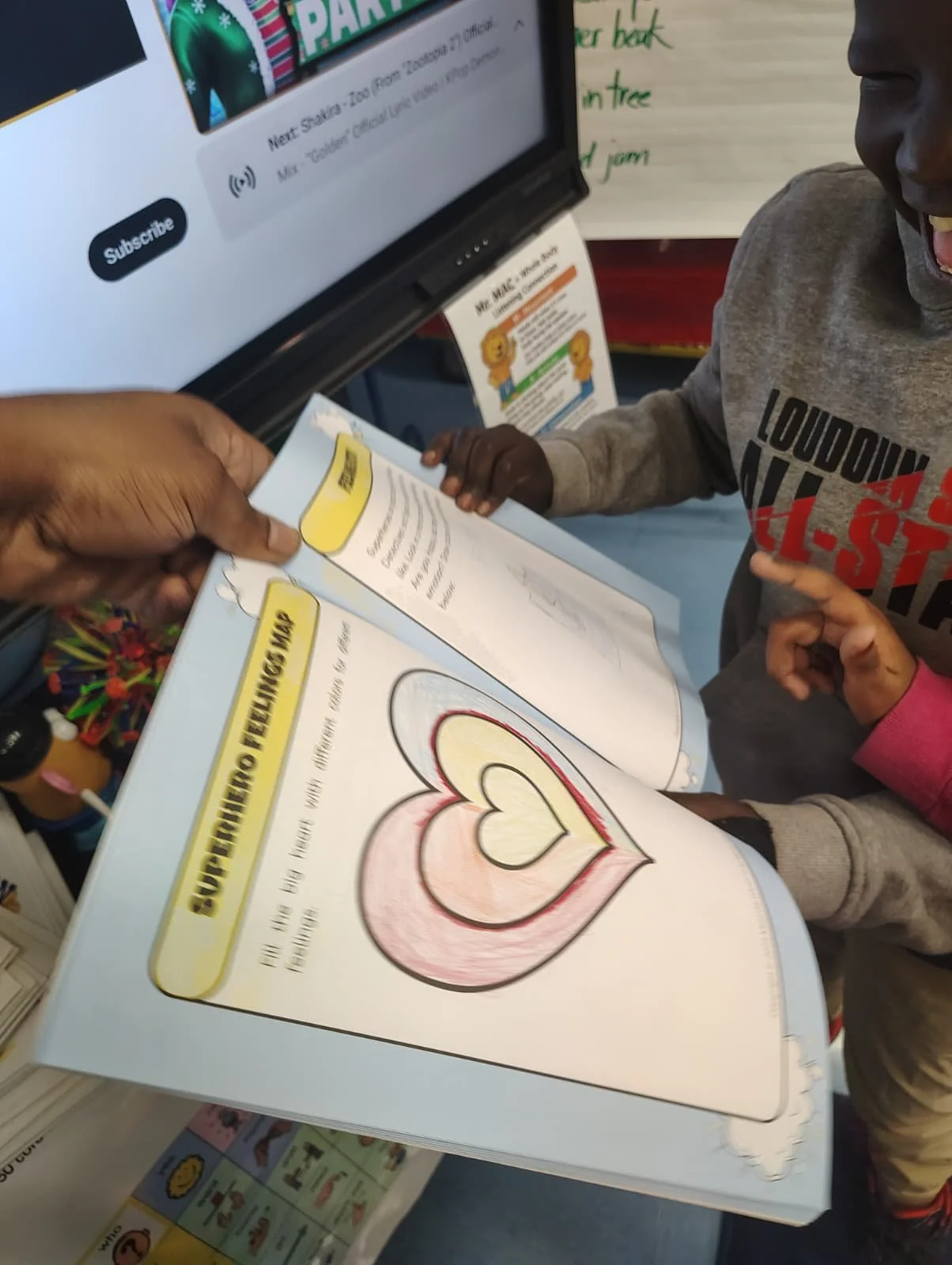 A child and an adult reading a book about the human heart, which is colorfully illustrated, in a classroom or bookstore setting.