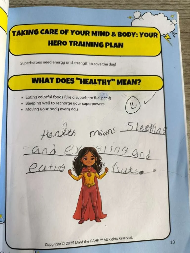 Page from a children's educational worksheet with a superhero theme. The worksheet includes a bright yellow title box that reads 'Taking Care of Your Mind & Body: Your Hero Training Plan.' It discusses what 'healthy' means, mentioning eating colorful