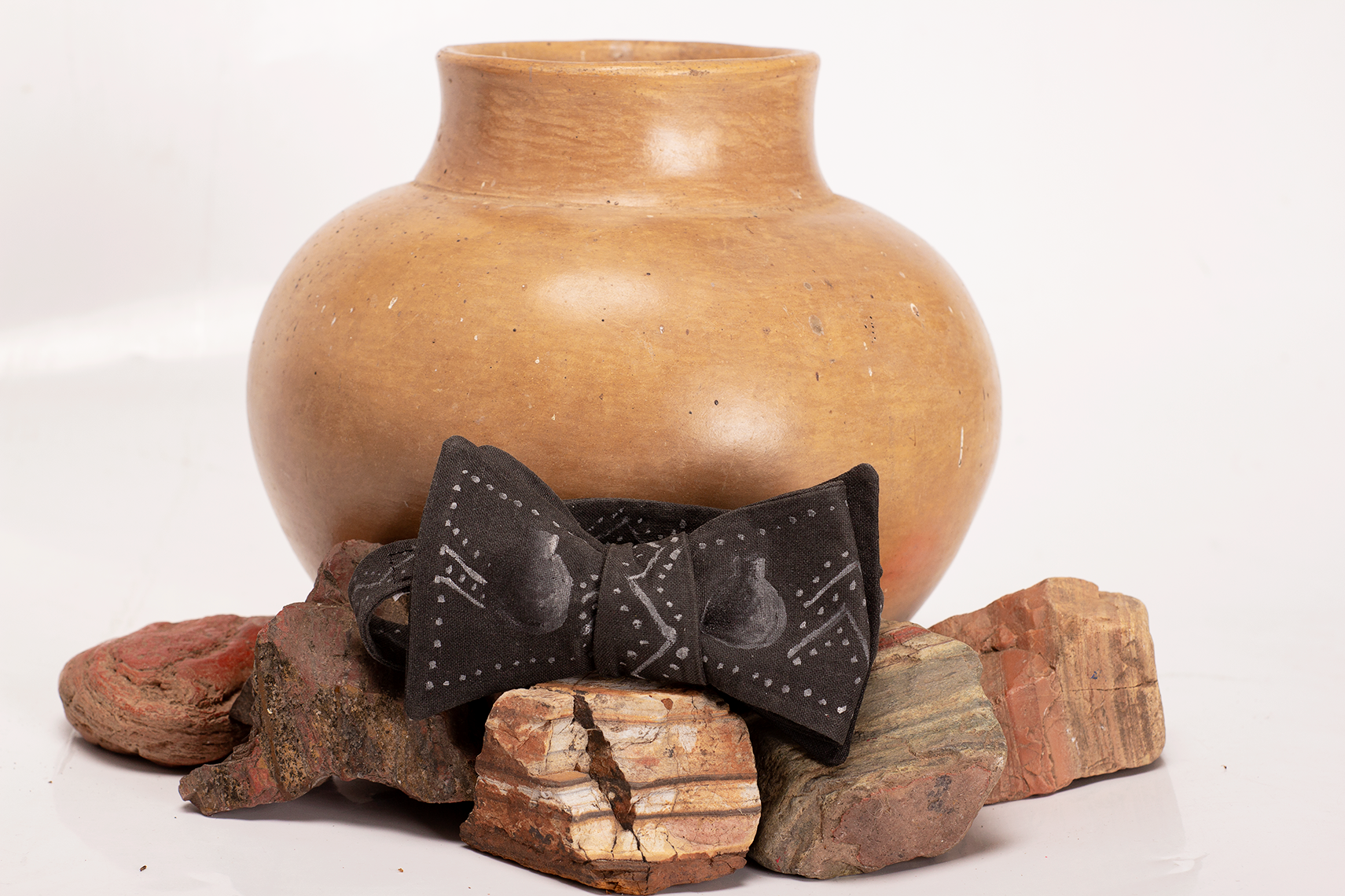 "Earth That Feeds Us" a black self-tied bow tie with traditional Zimbabwean patterns and a clay pot handpainted on it in white by Bernardo Marira