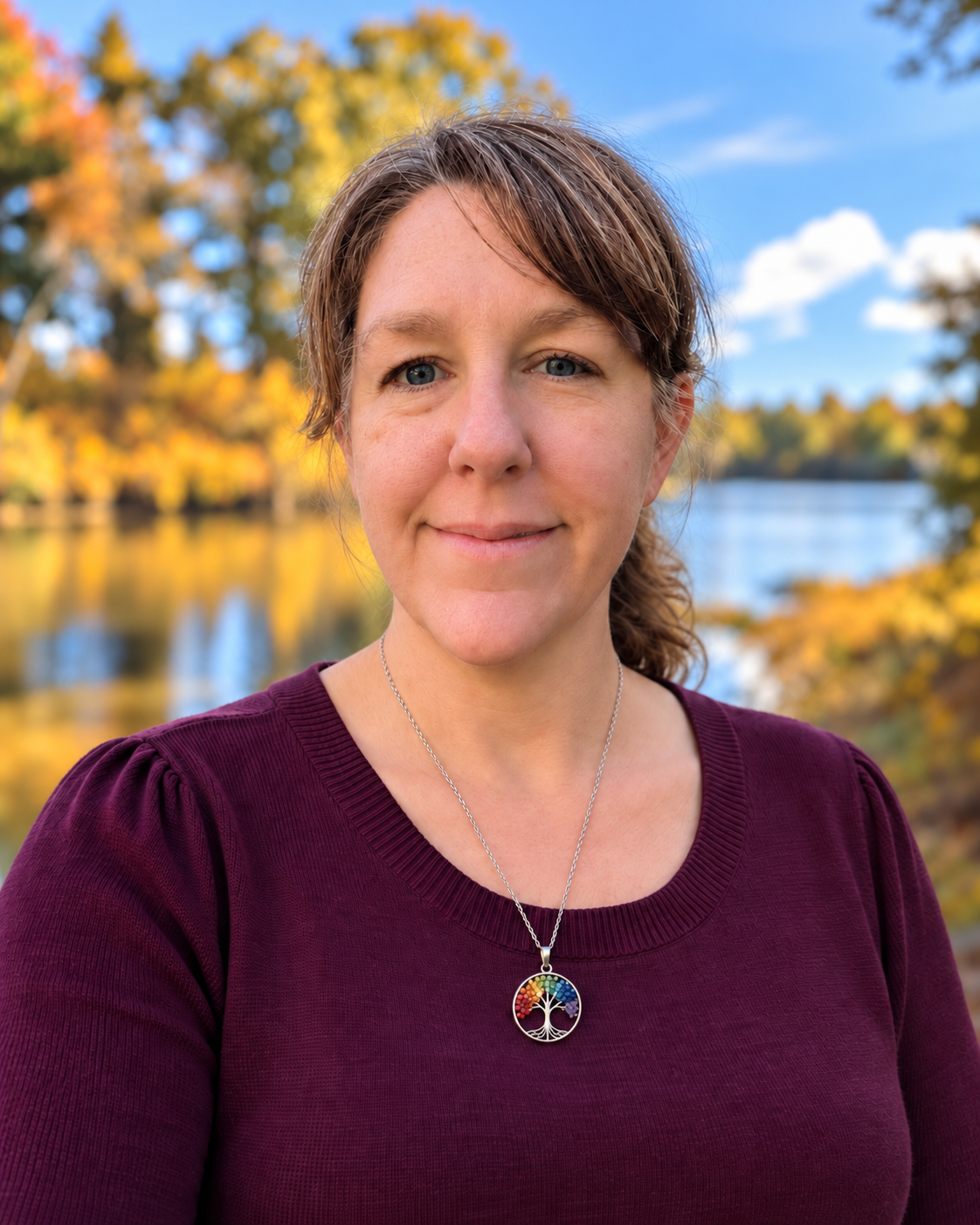A woman stands in front of a river in the fall.