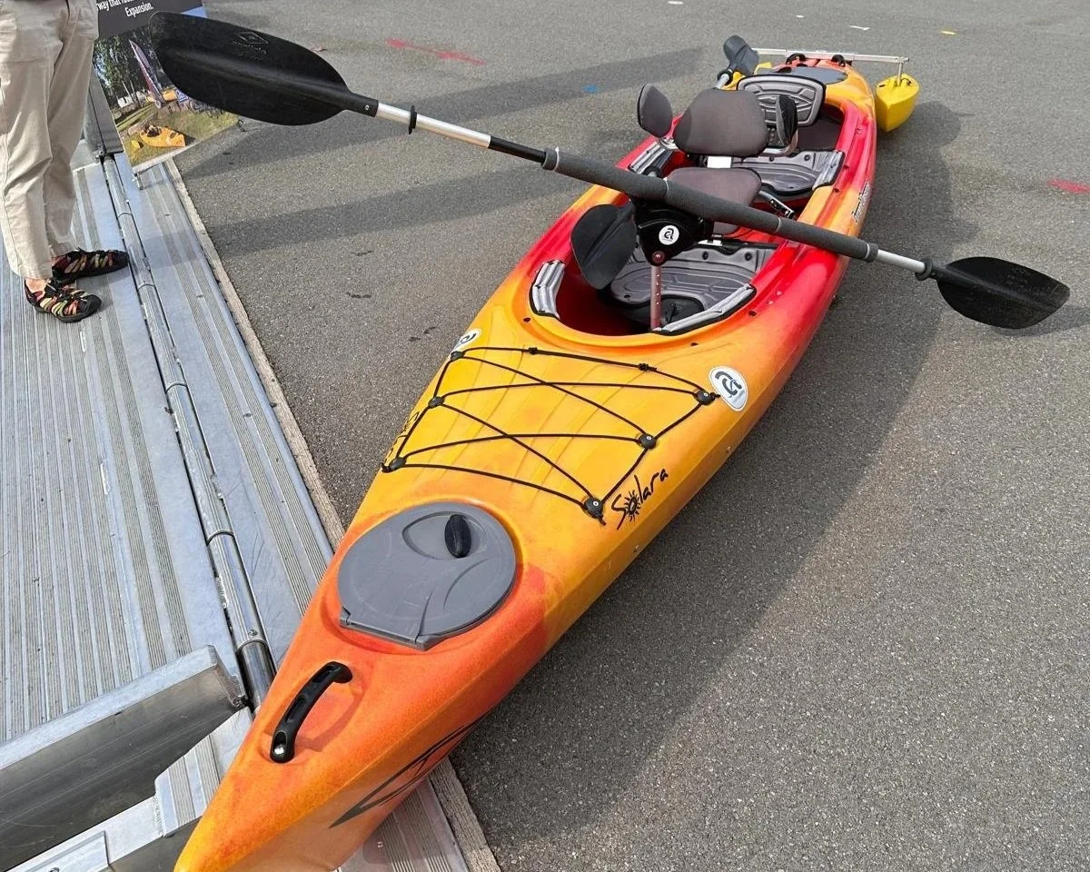 A bright orange tandem kayak sits on a cement surface.