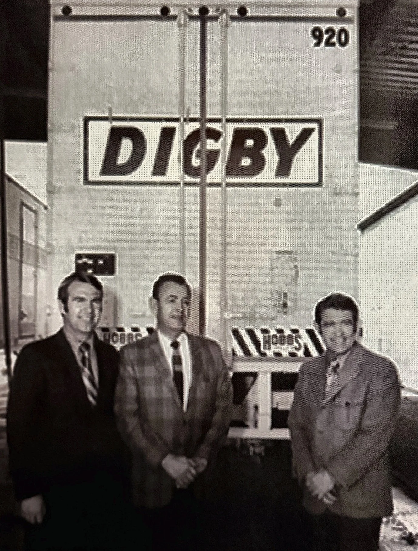 Three men in suits standing in front of a Digby trailer
