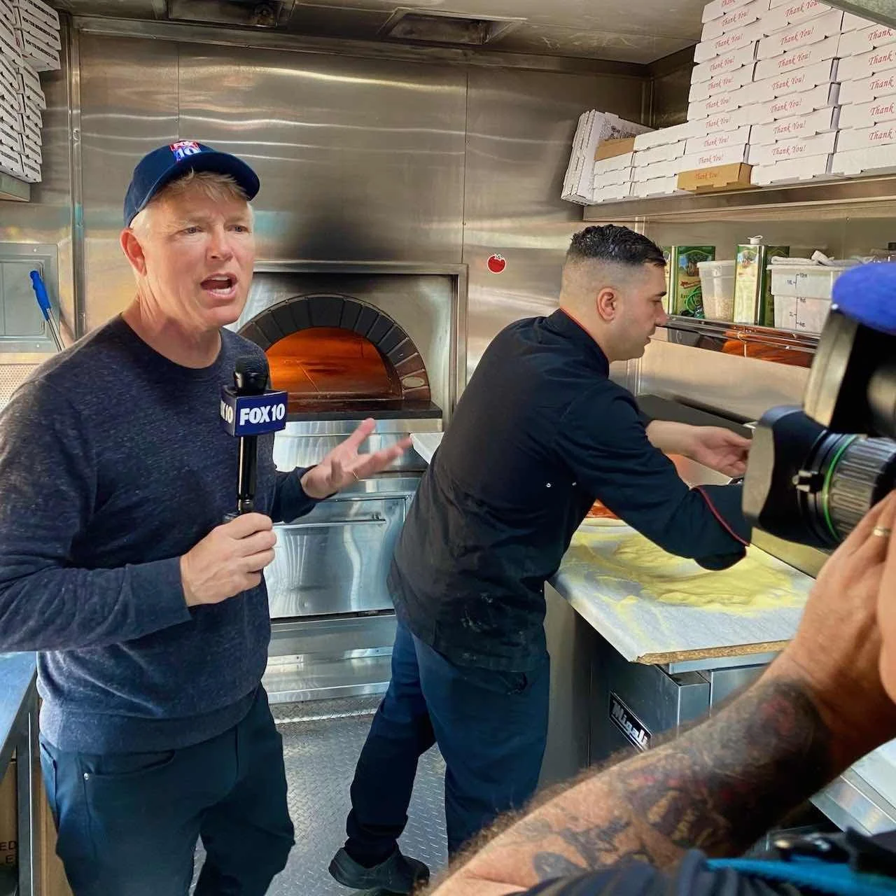 FOX 10 Phoenix reporter Cory McCloskey broadcasting live inside Re Di Roma food truck as pizzaiolo Oualid Ferhati prepares pizza.