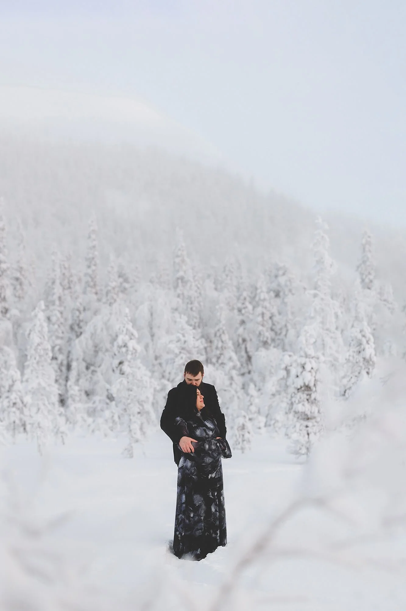 Marriage proposal in Rovaniemi. A couple standing in a snowy landscape with snow-covered trees in the background; the man is embracing the woman, who has her eyes closed.