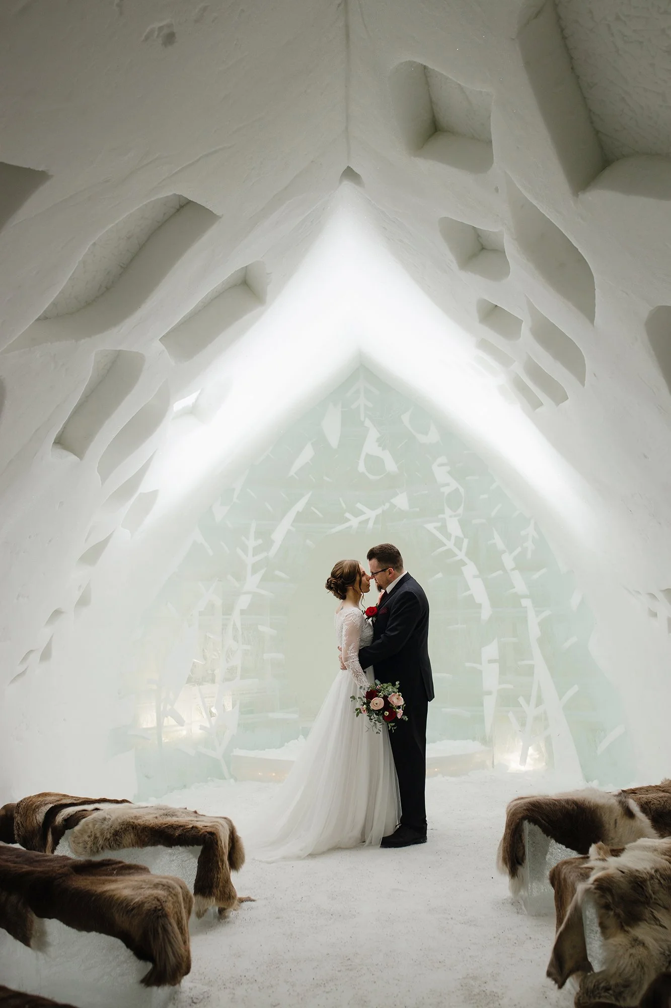 A bride and groom kissing inside an icy white Arctic ice cave, surrounded by puppies lying on the ground. Tina the Lapland Photographer takes amazing wedding photos in Rovaniemi and whole Lapland.