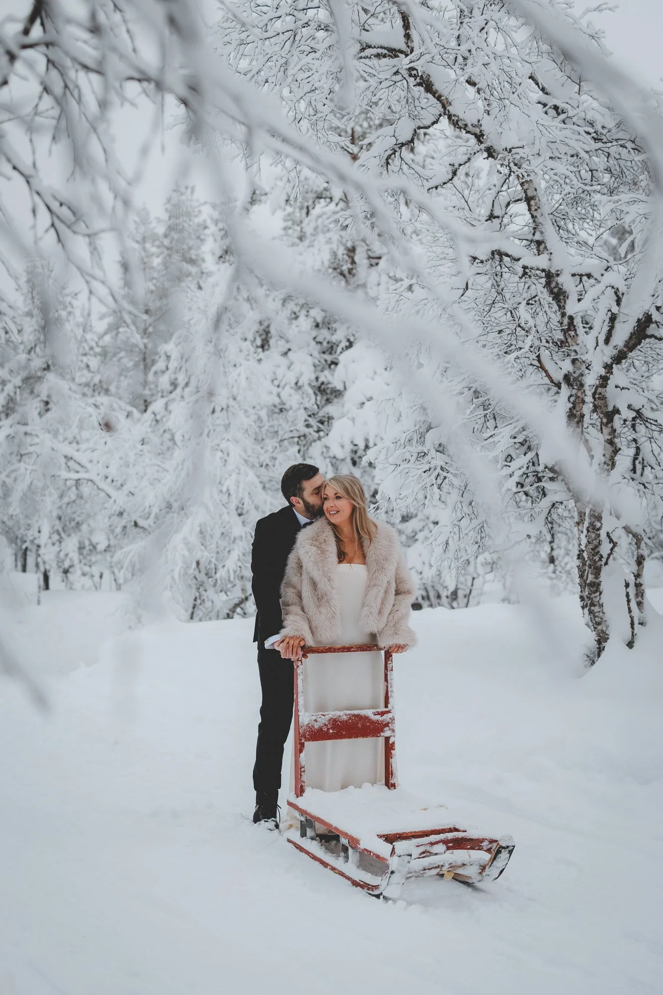 Wedding photos by Tina the Lapland Photographer. A couple dressed in formal winter clothing standing outdoors in a snowy landscape.