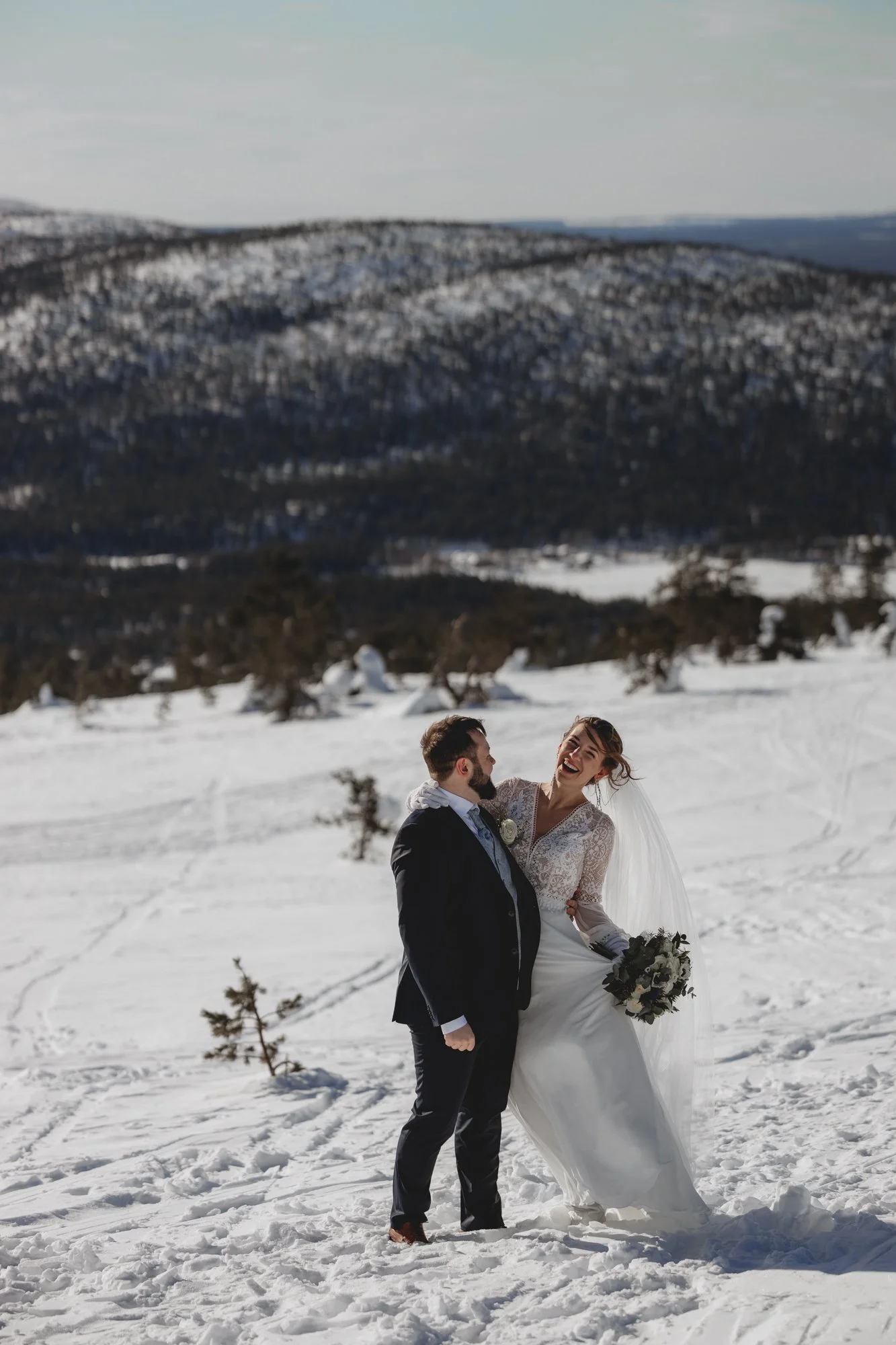 Lapland wedding. A bride and groom standing in a snowy landscape with snow-covered mountains in the background. 