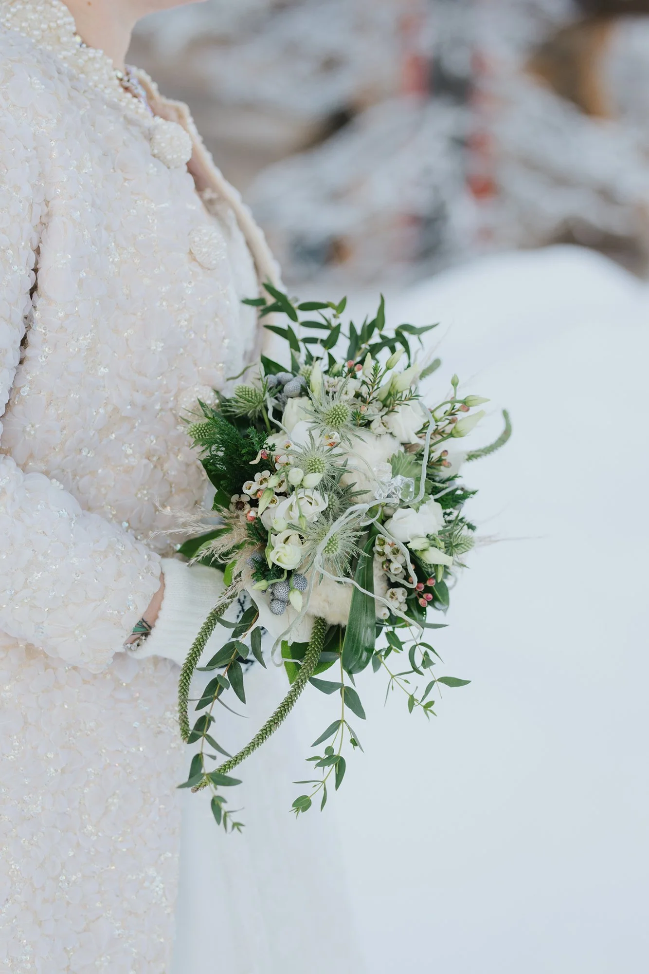 Wedding photoshoot in Lapland. A bride in a white dress holding a bouquet of white flowers and greenery, standing in a snowy outdoor setting.