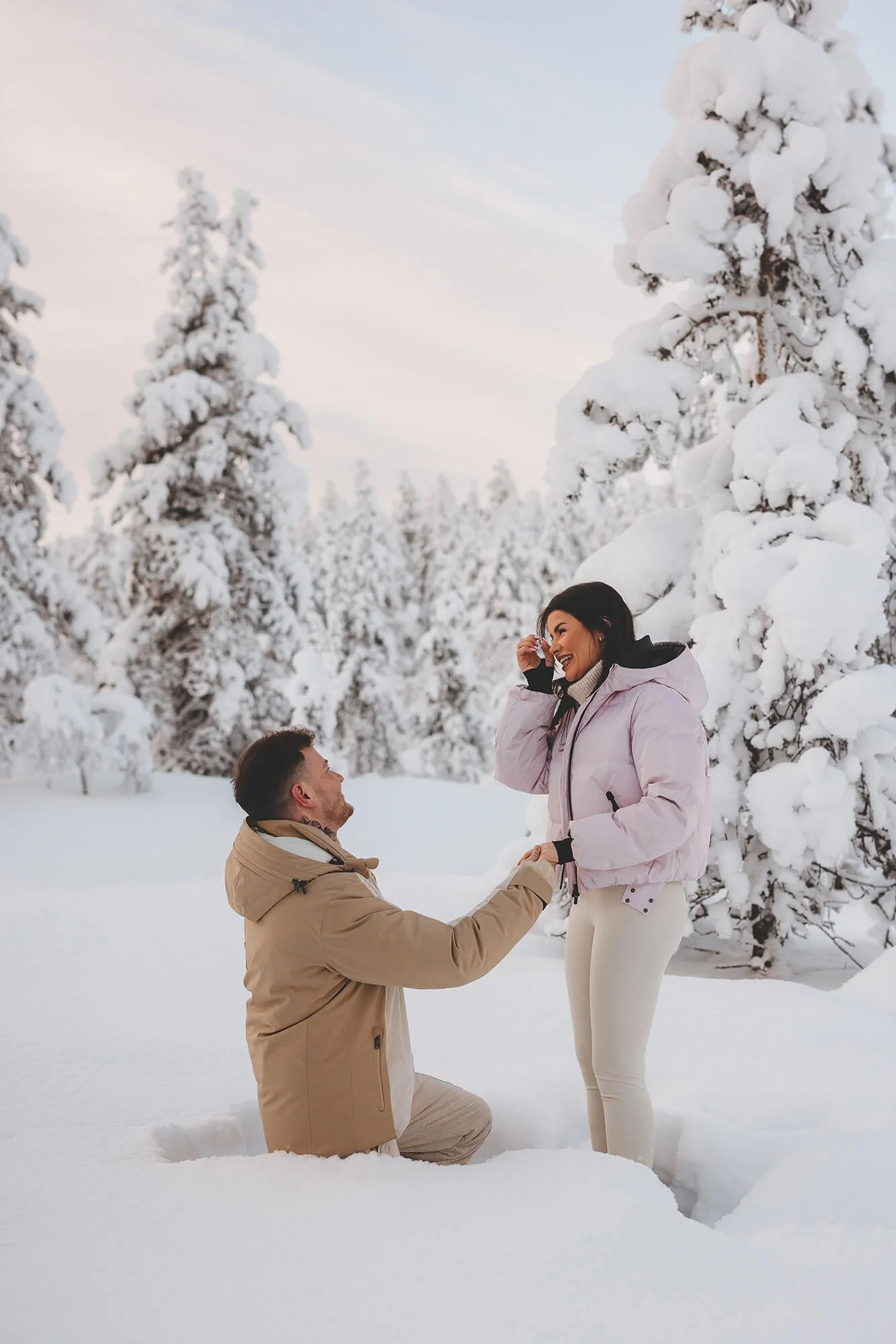 Marriage proposal photos. A man kneeling in the snow and proposing to a woman, who is smiling and holding his hand, in a snowy forest. 	
Elopement photographer Rovaniemi and Lapland. 