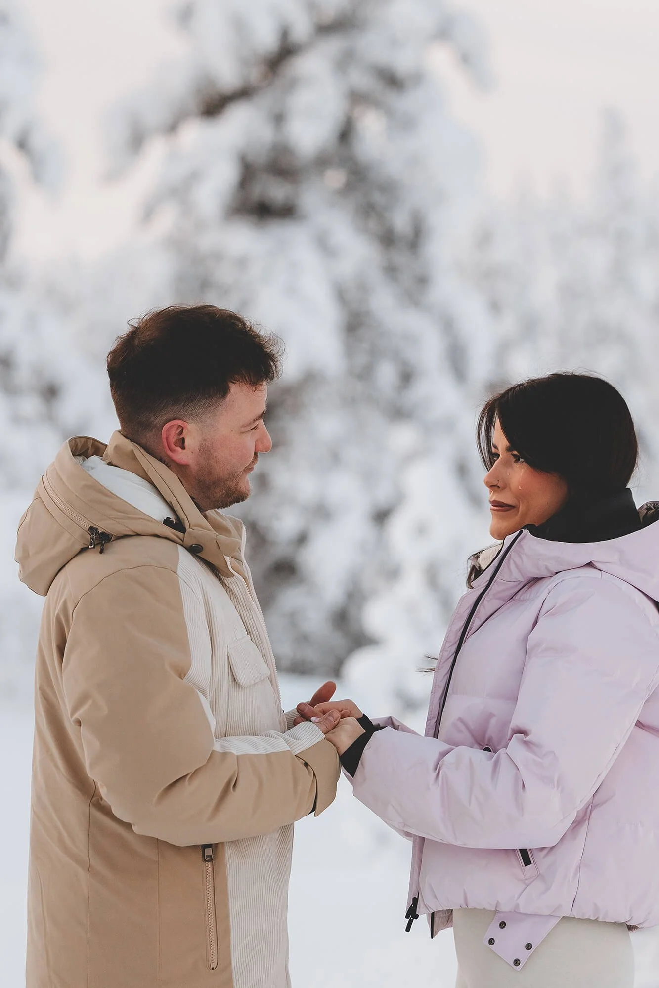 A couple exchanging wedding vows in a snowy outdoor setting, with trees covered in snow in the background.