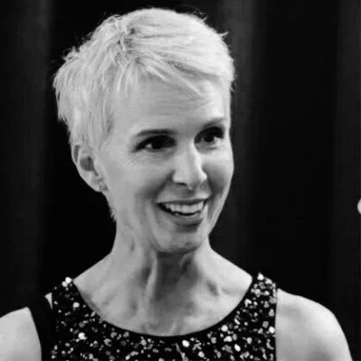 Black and white photo of a woman with short, light-colored hair wearing a sleeveless, sparkly top.