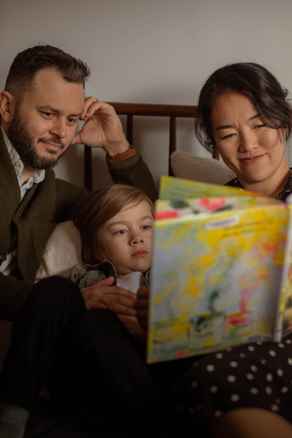 the cutest photo of a mom and dad reading with their son on their bed