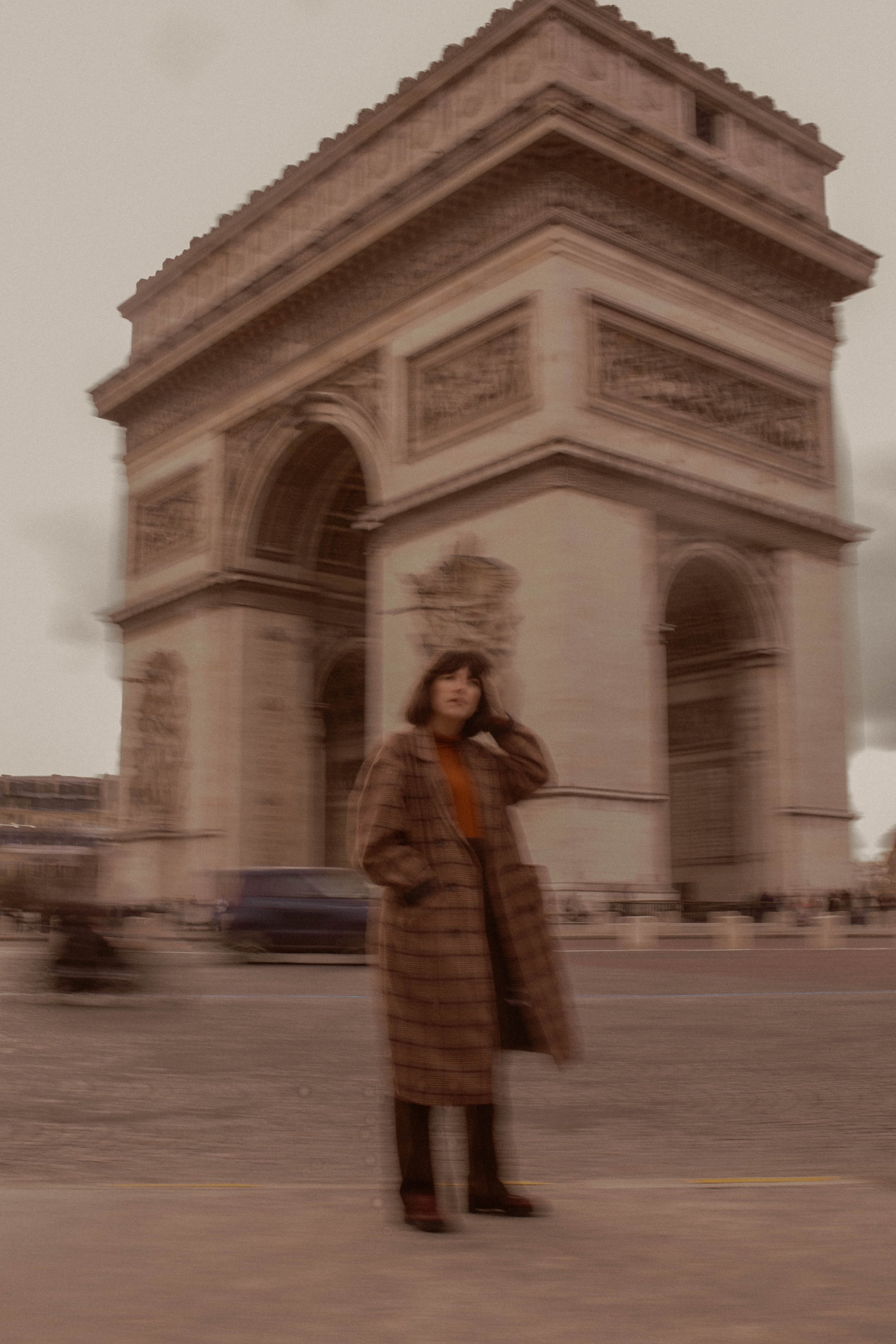 blurry image of woman in coat standing in front of arc de triumph in Paris