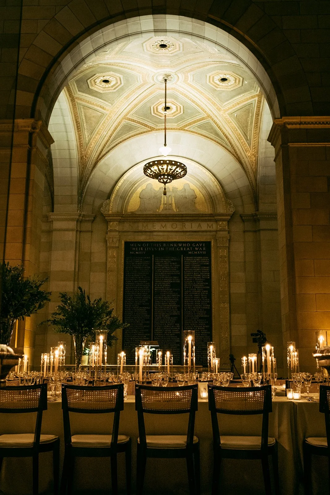 Elegant memorial hall with a decorated ceiling, large memorial plaque, and tables set for a formal event with candles and greenery.
