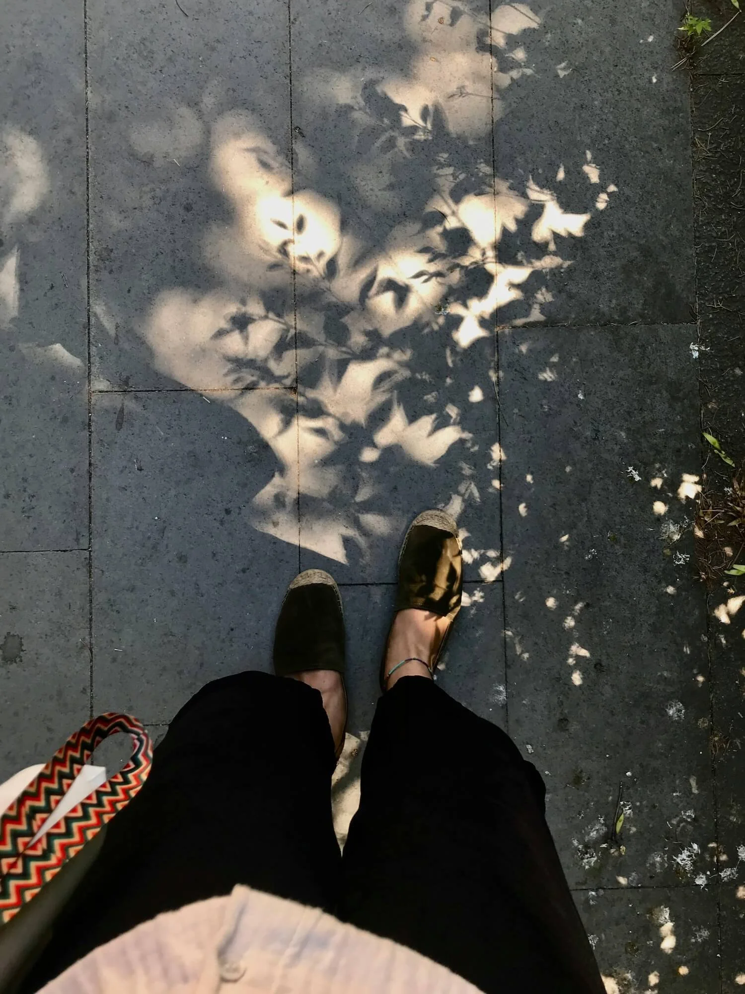 Woman standing in dappled light on a sidewalk