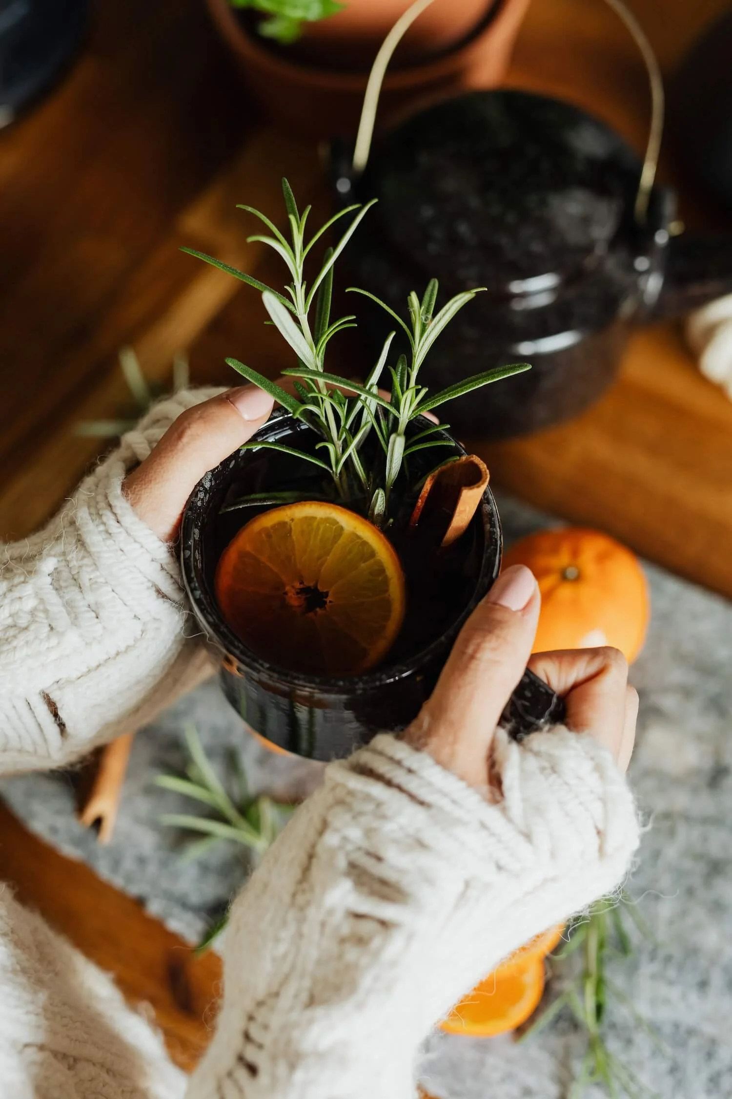 Hands hold an herbal infusion with orange and rosemary, suggesting nourishment as part of how to get out of survival mode.