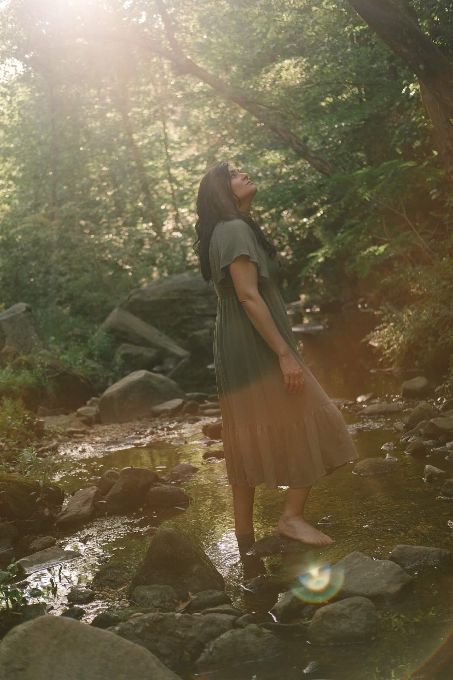 Kim Kimball gazes up in a sunlit forest, finding peace and guidance through professional Life Transition Coaching.