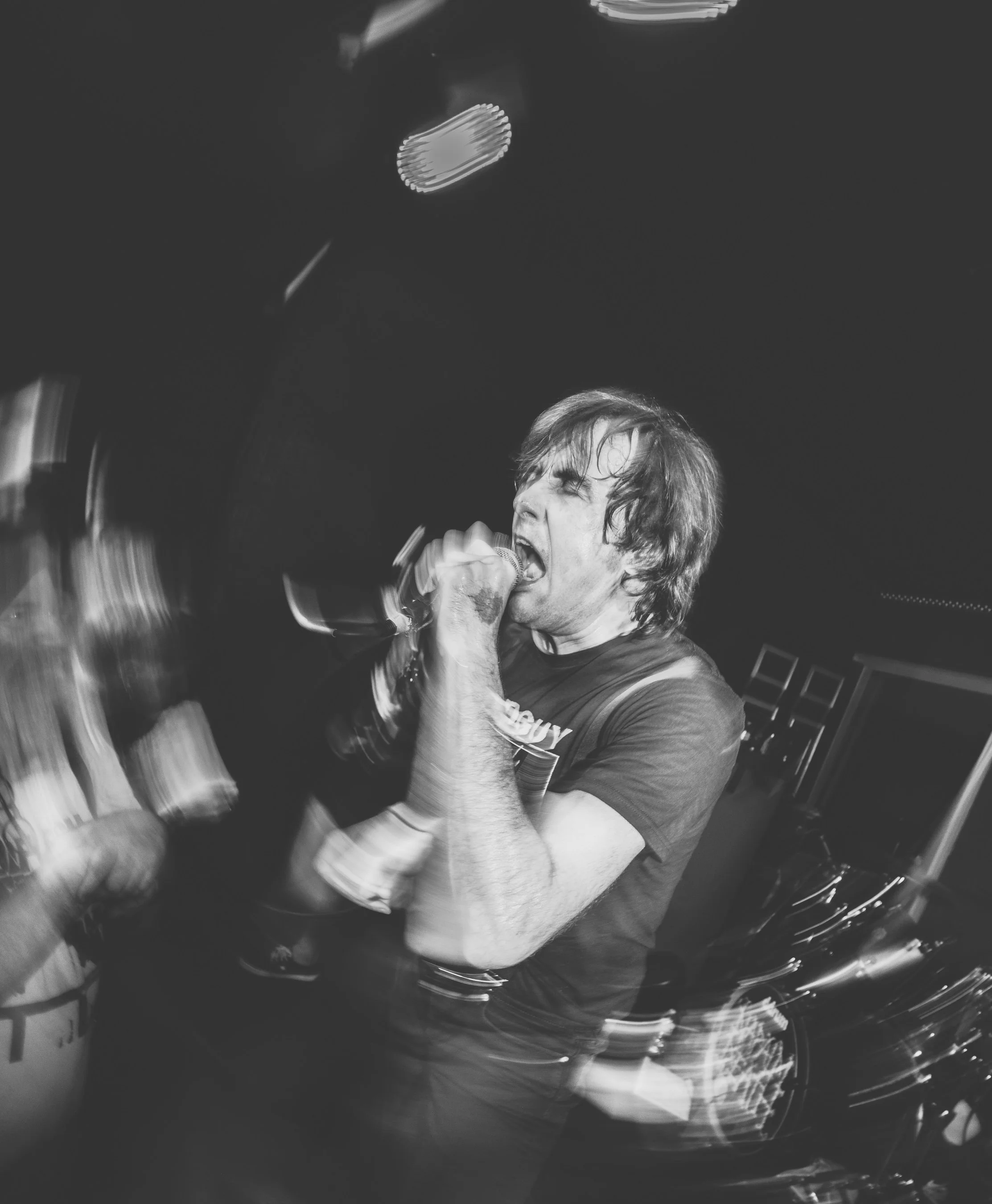 A person singing into a microphone while playing a guitar, captured in black and white with motion blur.