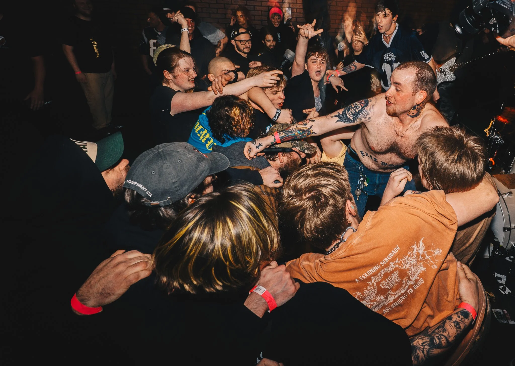 A crowd of people at a concert, with a shirtless singer with tattoos reaching out to the audience. The crowd appears excited and engaged.